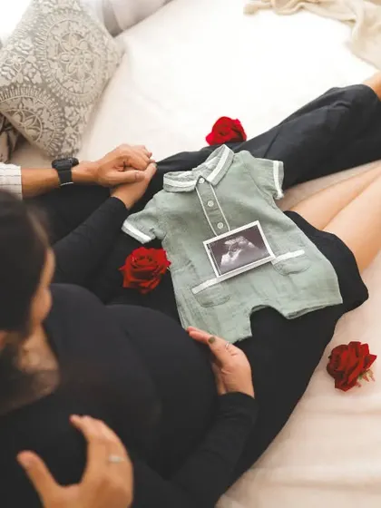 "Our little family in the making." This creative shot from above shows the couple holding hands on a bed, with a baby romper and ultrasound picture placed lovingly by the bump.