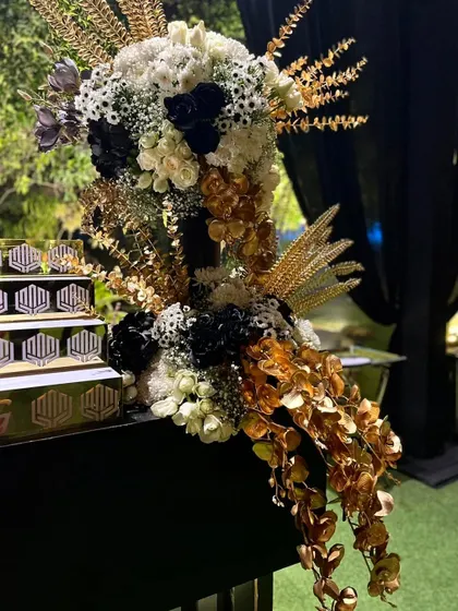 A detailed shot of the bar's floral arrangement, showing the intricate combination of textures and colors. The golden elements and feathers add a unique, glamorous touch to the classic black and white theme.