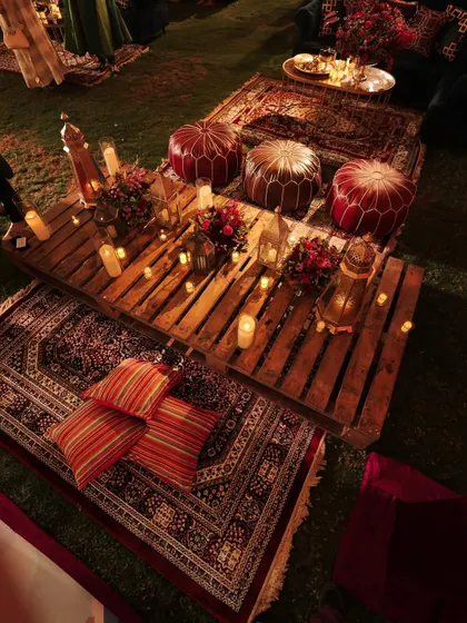 A full view of the picnic seating, with layered rugs, cushions, and ottomans creating a relaxed and bohemian vibe. The candlelight makes the space feel incredibly warm and intimate.