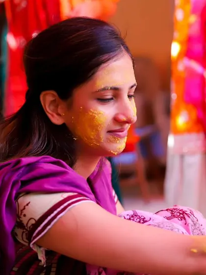 A serene and happy moment from the Haldi ceremony. The bride is smiling peacefully as turmeric is applied, surrounded by the vibrant colours of the celebration.