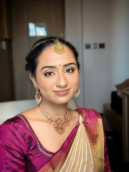 A portrait of a happy bride-to-be. The makeup is kept soft and natural, with a focus on glowing skin and a subtle definition on the eyes and lips to match the grace of her silk saree.