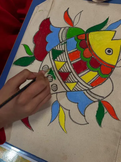 Watching a young artist fill in the vibrant colours of their Madhubani fish. Each child brings their own unique touch to these traditional designs.