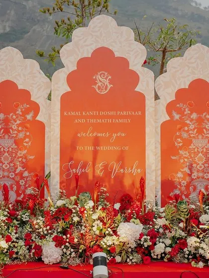 A beautiful welcome sign with Jharokha-shaped panels and a bed of red and white flowers.