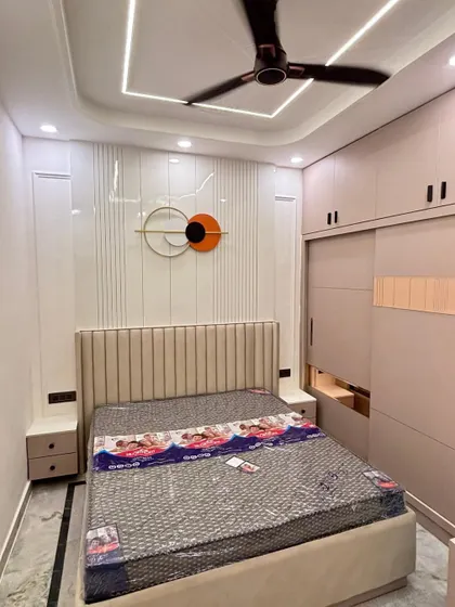 This bedroom features a vertically paneled headboard and a sliding wardrobe in a soft beige tone. The false ceiling with cove lighting adds to the room's modern and clean aesthetic.