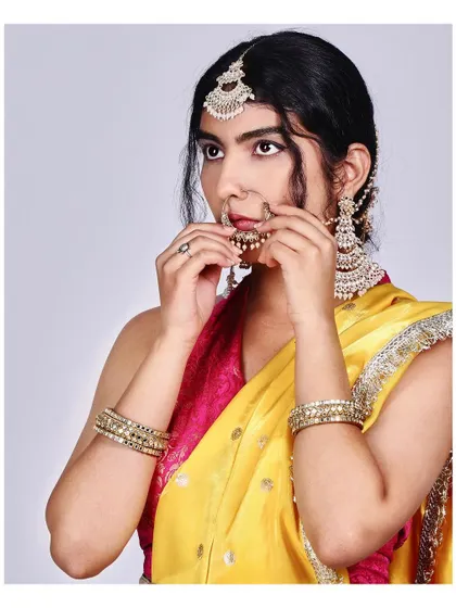 A candid moment of a model adjusting her nath (nose ring). This shot captures the small, intimate details of getting ready in traditional Indian attire.