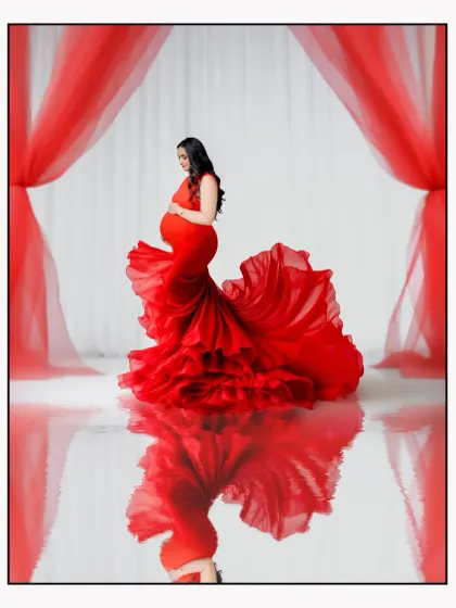 A dramatic solo portrait in our studio featuring a vibrant red maternity gown with a long, ruffled trail, creating a stunning reflection on the floor. This style is perfect for mothers-to-be who want a bold and glamorous photoshoot.