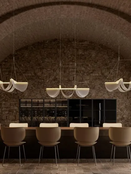 A row of Drape Lights by Jamie Wolfond for Moooi illuminates a long dining table in a rustic, vaulted cellar. The design, like a perfectly draped fabric, brings effortless grace and warmth.