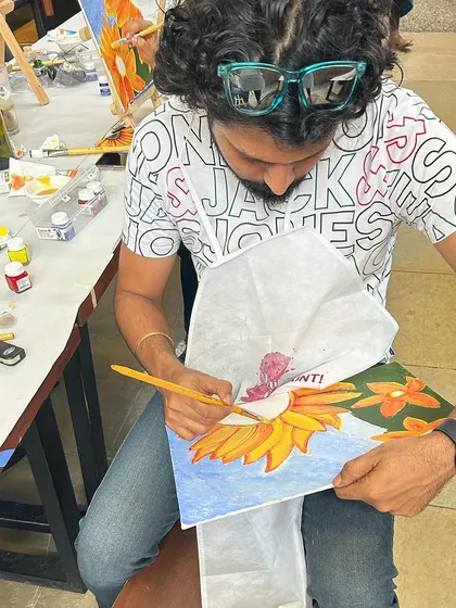 A participant at the EYGBS event carefully painting a sunflower. The concentration and enjoyment are clear.