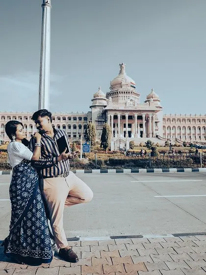 A duplicate of a grand wide shot of a couple walking hand-in-hand in front of the magnificent Vidhana Soudha.