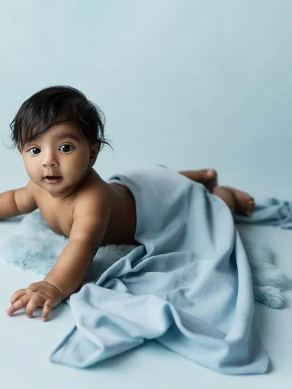 A playful shot of a baby under a light blue blanket, peeking out with a curious expression. A fun and creative idea for a sitter session.