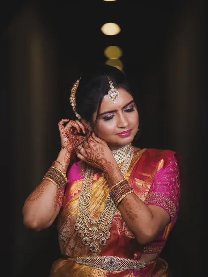This look focuses on the rich details of a South Indian bride. The makeup features dramatic eyes and a soft pink lip, perfectly complementing her intricate diamond jewellery and the vibrant colours of her saree.