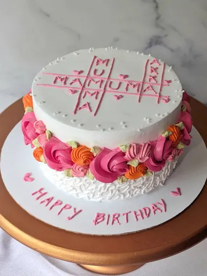 A sweet whipped cream cake with a "MAMA" crossword puzzle design. The sides are decorated with colorful piped rosettes.