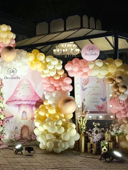 A corner of the celebration featuring a whimsical mushroom house prop, a personalized welcome sign, and a cascade of pastel balloons.