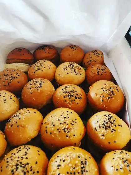 A box of freshly made veg sliders, ready for delivery to a birthday party. Topped with sesame seeds, these mini burgers are a convenient and popular appetizer.