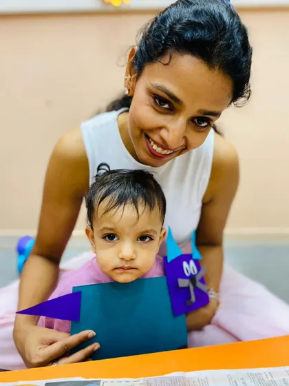 A smiling mother and her child hold up their craft project, a testament to the joyful learning environment we create.