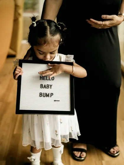 A close up shot of the little girl carefully holding the "Hello Baby Bump" sign. This focuses on her role as the big sister and her connection to the new baby.