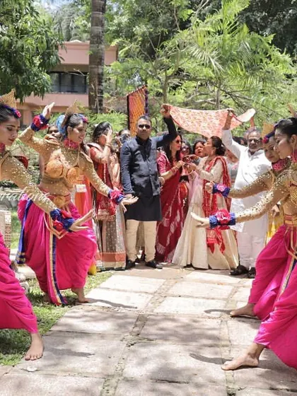 A joyous daytime function entry for the Bhaat ceremony at a Goa wedding. The traditional costumes of the dancers pop against the lush green background, creating a beautiful scene.