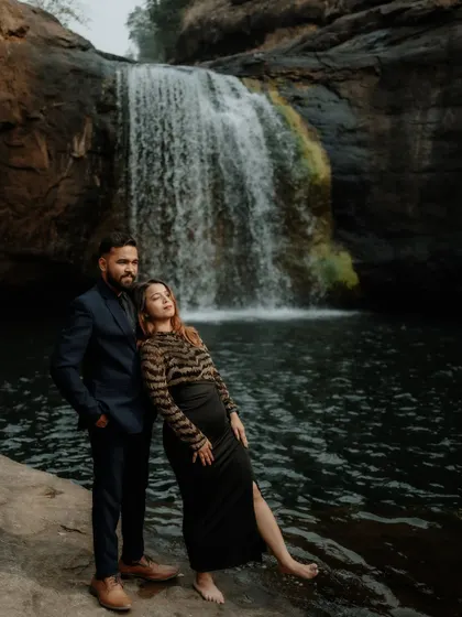 A stylish pose by the waterfall, showcasing the couple's attire and the beautiful natural scenery.