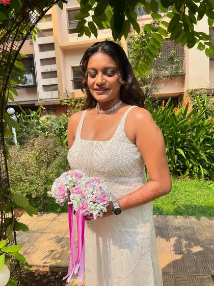 A beautiful outdoor shot. The natural greenery provides a stunning backdrop for her elegant white gown and flawless makeup.