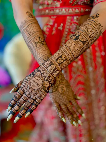 A crossed-arm pose showing the full view of the personalized "TS" and "Sutej" mehendi. The dark henna paste promises a rich and beautiful stain.