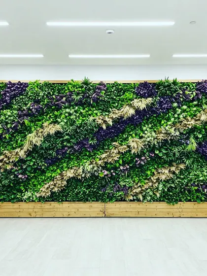 This artificial green wall features a striking diagonal pattern, using purple and light-colored foliage to create contrast against the green. The wooden base adds a natural finishing touch.