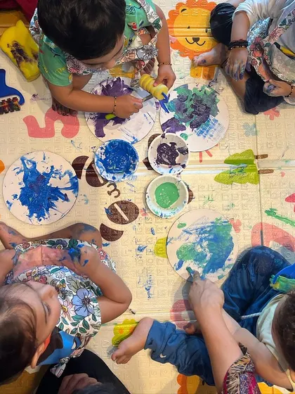 An overhead view of a collaborative art moment. Our sessions encourage toddlers to create alongside one another, observing and sharing the experience. Here, they are exploring different ways to apply paint to their own paper plates.
