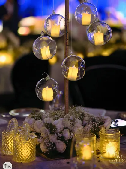 An elegant and intimate tablescape detail, with hanging glass globes holding candles that cast a magical glow over a centerpiece of baby's breath and white roses.