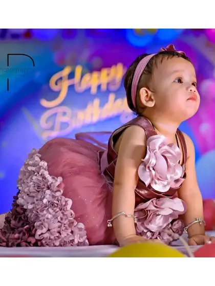 The birthday girl looking up in wonder at her party, dressed in a beautiful ruffled pink dress against a vibrant, colorful backdrop.