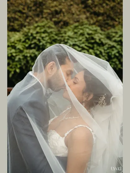 A timeless and romantic close-up of a bride and groom sharing a kiss under a delicate white veil. This intimate portrait focuses on the pure emotion and connection between the couple, creating a soft and dreamy wedding photograph.