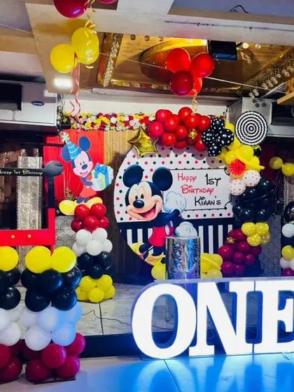 A large-scale Mickey Mouse first birthday party. The setup features a custom backdrop, balloon columns, and a giant light-up "ONE" sign.