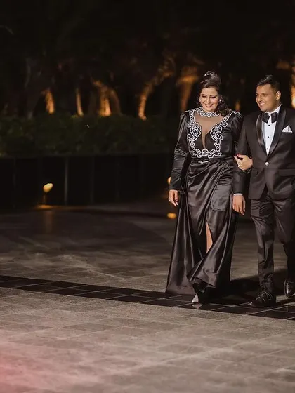 A classic shot of the couple walking arm-in-arm at their reception venue at night. They look elegant and happy.