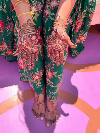 A lovely shot of a client's hands and feet, both adorned with henna. The feet have a simple, minimal design that complements the more intricate hand mehendi.