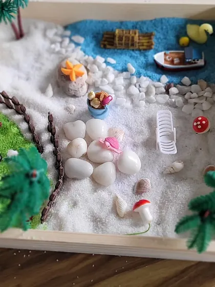 A tranquil beach scene comes to life with white sand, pebbles, and tiny palm trees. This workshop is a form of play that quietly teaches the principles of balance and composition.