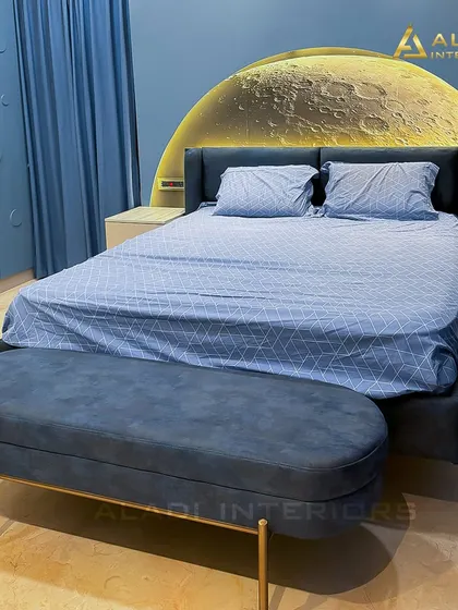 A close-up of the celestial-themed bed, showing the detail of the backlit moon headboard and the plush blue velvet bench at the foot of the bed.