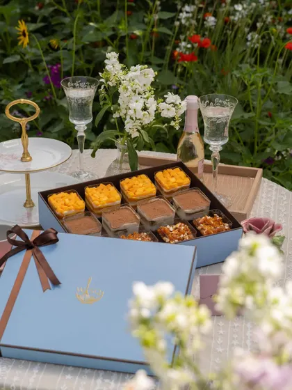 Our 12-piece dessert cup box, perfect for hosting a party or as a generous gift. This assortment includes our Mango & Cream Cheese Trifle, Classic Tiramisu, and Chocolate & Caramel Trifle, set against a beautiful garden backdrop.