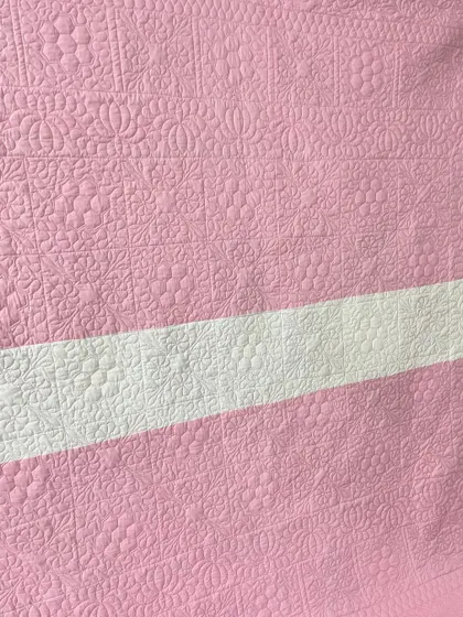 A close-up of the intricate quilting on the back of the pink hexagon quilt.
