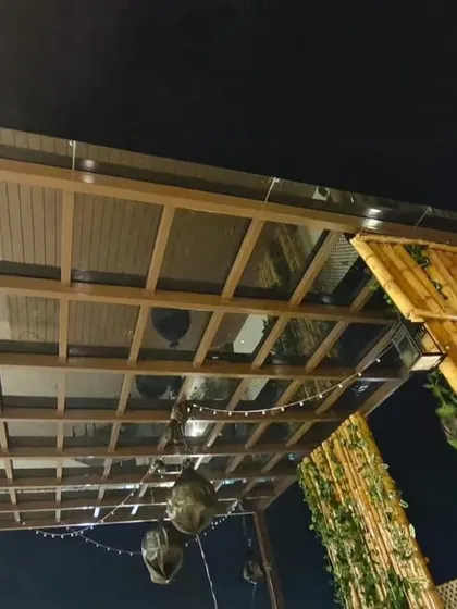 A glass pergola seen at night, with ambient string lights creating a warm and inviting atmosphere. This project at Swiss Town, Bangalore, combines a metal frame with a bamboo privacy screen for a rustic-modern look.