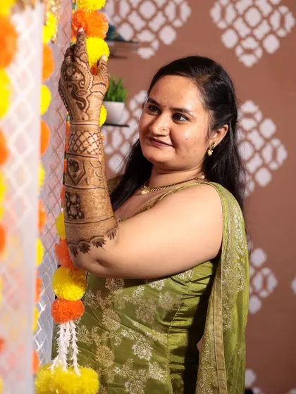 A happy client posing with her beautiful full-arm mehndi. The festive marigold decorations in the background add to the cheerful vibe.