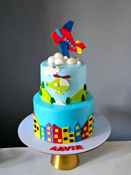 An airplane-themed cake soaring over a city skyline. This two-tier whipped cream cake is bright and colorful, with handmade fondant planes and helicopters.