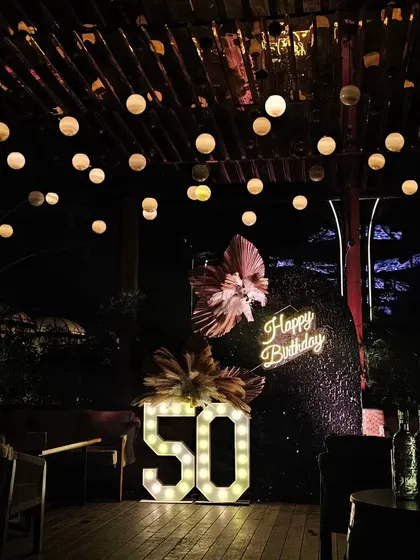 A close-up of the 50th birthday photo backdrop. The black sequin wall, neon sign, and pampas arrangements look stunning against the night sky.