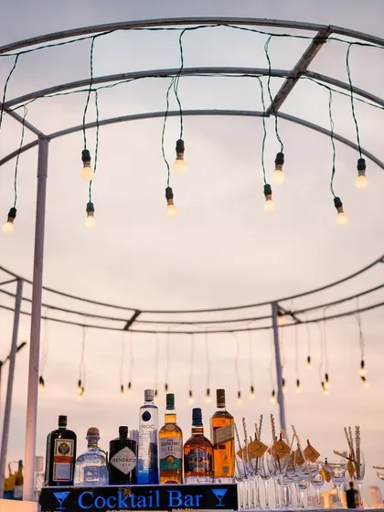A beautiful shot of the cocktail bar set up for a sundowner event in Goa, with fairy lights twinkling against the twilight sky.
