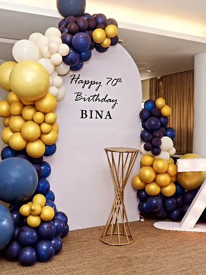Celebrating 70 and fabulous! This simple and elegant coustamised decor for a 70th birthday features a modern arched backdrop and a stylish balloon arrangement in mustard yellow and blue.
