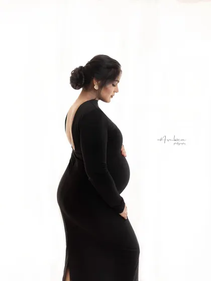 The elegance of a backless black gown is showcased in this side profile portrait. The clean white background puts all the focus on her form, creating a sophisticated and modern maternity photograph.