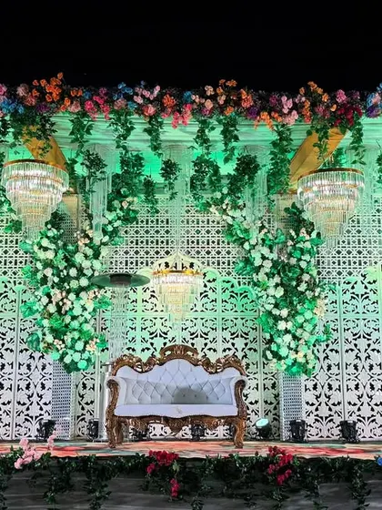 A full view of the green and white themed wedding stage. The symmetrical design with a central sofa, flanked by floral pillars and chandeliers, provides a balanced and picturesque setting.