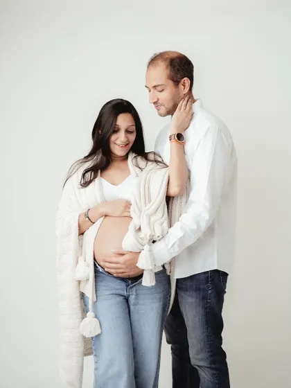This full-length shot captures the couple's anticipation. The simple, light-filled studio setting keeps the focus on their connection and the beautiful baby bump.