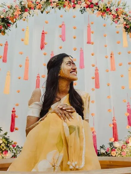 The bride looks up with a joyful expression as she is covered in turmeric paste during her Haldi ceremony.
