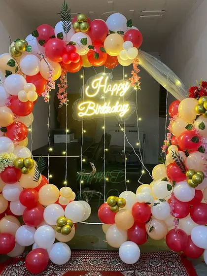 A warm and inviting birthday balloon ring in red, peach, and white, with a neon sign and fairy lights.