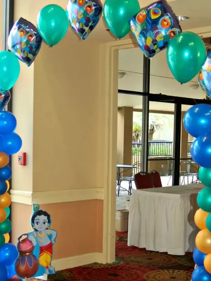 An entrance arch for a Krishna-themed party, using blue, green, and orange balloons, peacock feather foil balloons, and a Krishna cutout.