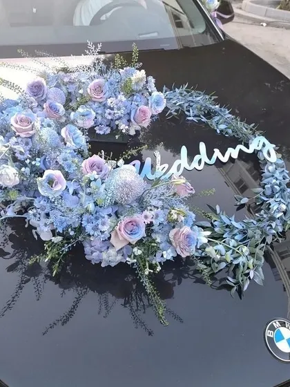 A crescent-shaped fresh flower arrangement for a BMW wedding car. The cool tones of the blue and purple flowers create a sophisticated and modern look.