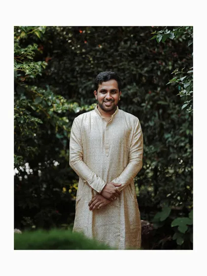A simple, elegant portrait of the groom in his Haldi attire, standing in a lush green garden.